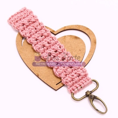 Pulseira artesanal em crochê rosa com fecho metálico dourado sobre base de madeira em forma de coração