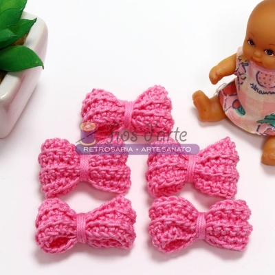 Quatro laços tricotados cor-de-rosa com planta e boneca ao lado