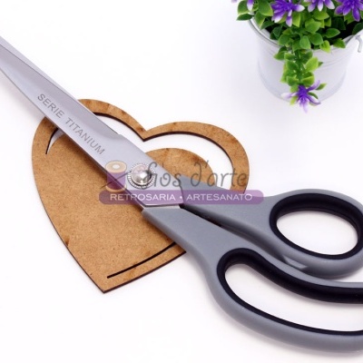 Tesoura cinzenta com lâmina metálica sobre suporte em forma de coração de madeira, ao lado de vaso com flores roxas