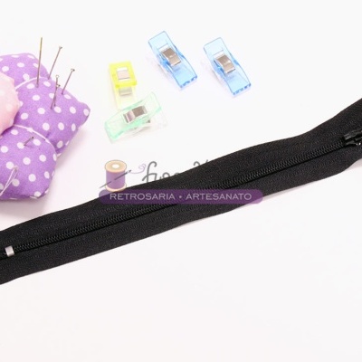 Dois fechos de correr pretos com dentes pequenos, alfineteiro roxo com bolinhas e pregadores coloridos em fundo branco