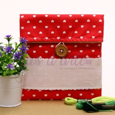 Envelope artesanal vermelho com corações brancos e botão de madeira, com plantas e linhas verdes ao lado