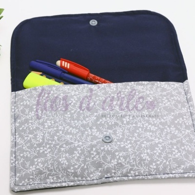 Estojo de tecido cinza com padrão floral branco e interior azul escuro aberto com canetas dentro