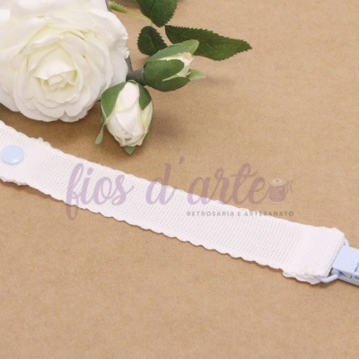 Prendedor de tecido branco com clip azul claro e botão branco sobre superfície bege com flores brancas