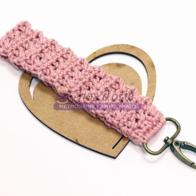 Chaveiro em crochet rosa com fecho metálico sobre suporte de madeira em forma de coração