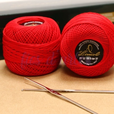 Dois novelos de linha vermelha para croché e duas agulhas metálicas sobre superfície bege