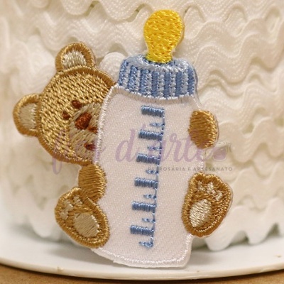 Bordado de urso a segurar biberão num tecido branco com textura ondulada