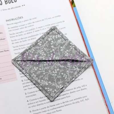 Guardanapo de tecido cinza com padrão floral branco sobre livro aberto com texto em português.