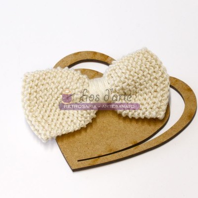 Laço de lã branco em base de madeira em forma de corações entrelaçados.