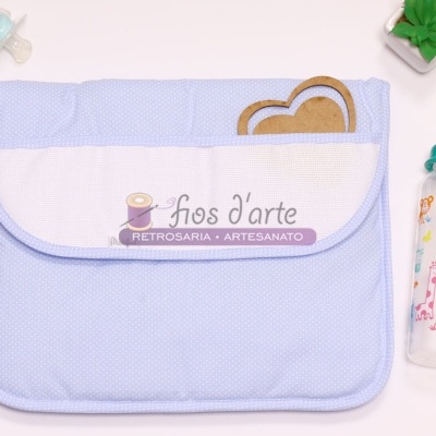 Muda-fraldas azul claro com bolso branco e marca Fios d'arte, chupeta azul e biberão com animais