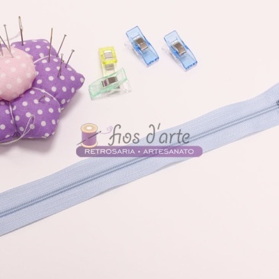 Alfineteiros, mola de correr azul clara e quatro clipes de tecido coloridos sobre fundo branco