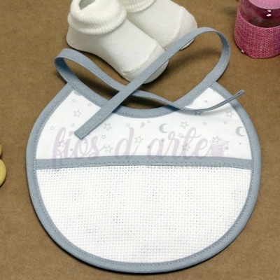 Babete branco com acabamento cinza, meia branca, anéis de madeira e frascos coloridos sobre superfície castanha