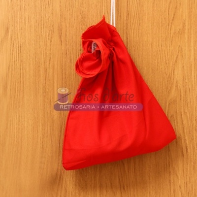 Saco de tecido vermelho pendurado numa porta de madeira clara