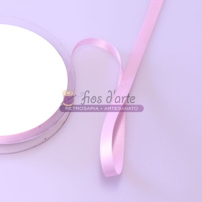 Rolo de fita cetim rosa claro com fita desenrolada sobre fundo lilás