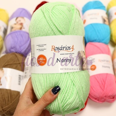 Novelo de lã verde claro Rosários 4 Nanny com outros novelos coloridos ao fundo.