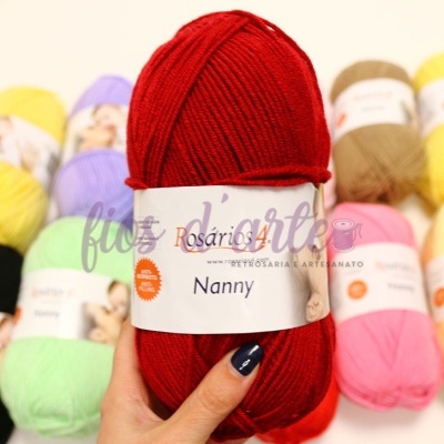 Novelo de lã vermelho da Rosário Nanny segurado por mão azul, rodeado de novelos coloridos.