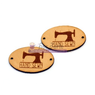 Dois rótulos ovais em madeira clara com desenho de máquina de costura e texto HAND SEWN