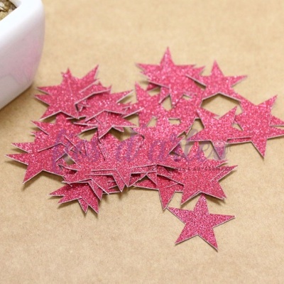 Estrelas decorativas cor-de-rosa com brilho sobre superfície castanha perto de vaso branco.