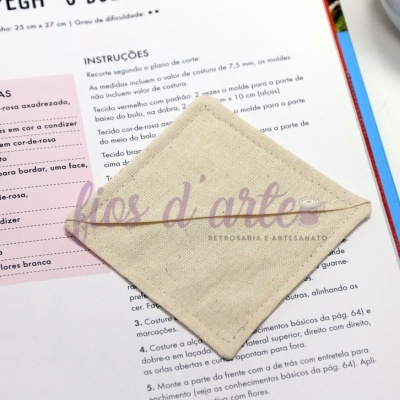 Máscara de tecido bege claro quadrada sobre livro aberto com texto em português