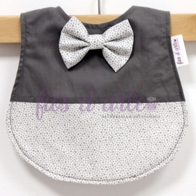 Babete para bebé cinzento e branco com laço pendurado numa cabide de madeira