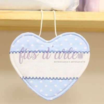Almofada em forma de coração azul claro com bolinhas brancas pendurada numa prateleira de madeira
