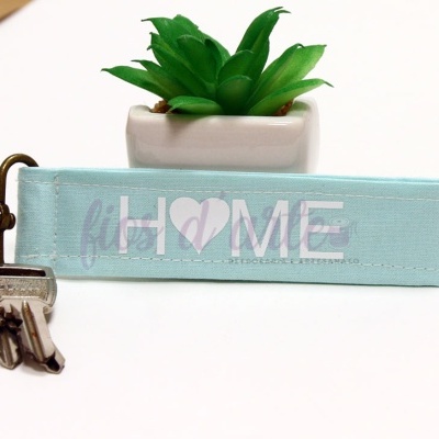 Chaveiro tecido azul claro com texto HOME e coração, chaves e planta artificial