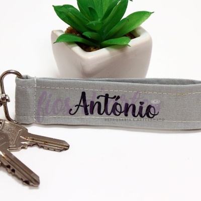 Chaveiro com alça de tecido cinzento claro com nome António e chaves junto a vaso branco com planta