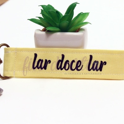 Chaveiro amarelo com texto 'lar doce lar' e planta suculenta em vaso branco