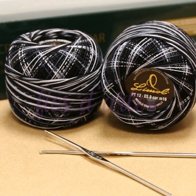 Dois novelos de fio para crochet preto e branco com agulhas metálicas sobre superfície bege