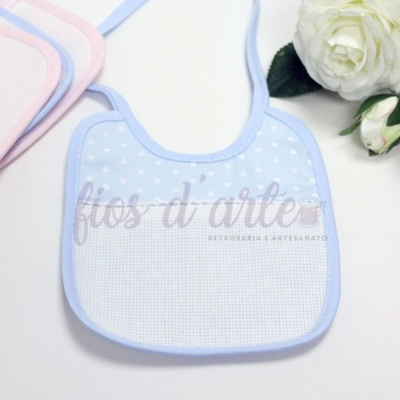 Babete para bebé azul com corações brancos e borda azul junto a rosas brancas.