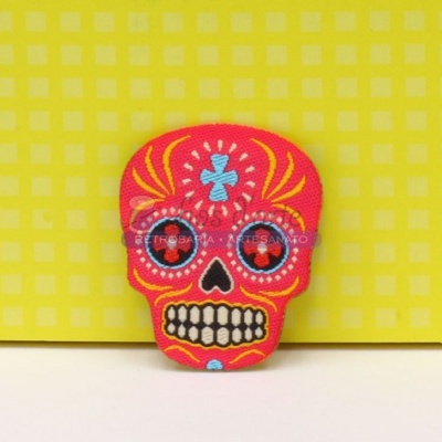 Alfinete decorativo em forma de caveira colorida sobre fundo amarelo quadriculado
