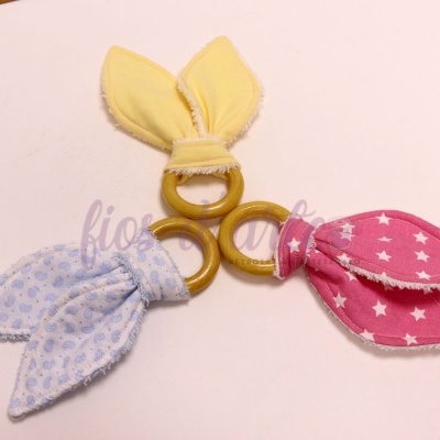 Três mordedores de madeira com tecido colorido em forma de orelhas.