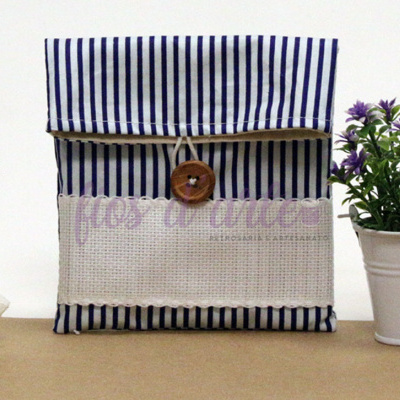 Bolsa de tecido riscada azul e branca com botão de madeira, rosa branca e vaso com flores roxas
