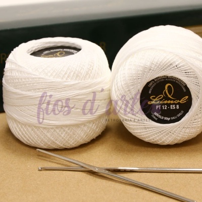 Dois novelos de linha branca para crochê com agulhas de metal e embalagem preta