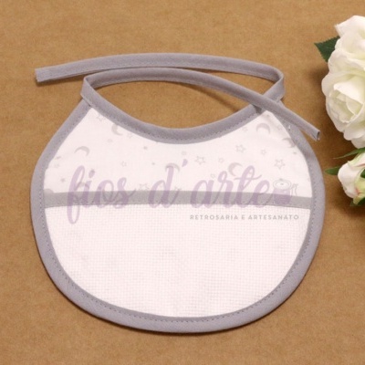 Babete branco com bordas cinzentas e padrão de estrelas e luas ao lado de flores brancas