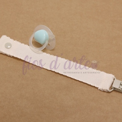 Prendedor de chupeta bege com chupeta azul e transparente sobre fundo castanho