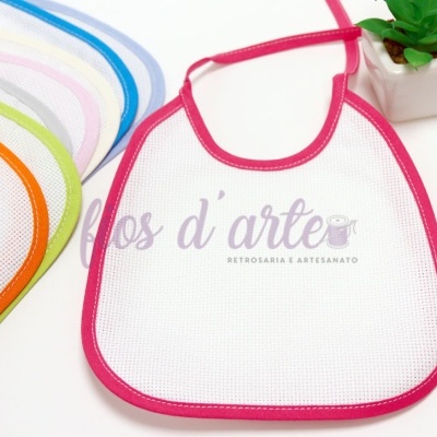 Babete branco com borda rosa e outros babetes coloridos ao lado de vaso com planta