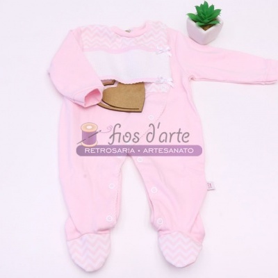 Pijama cor-de-rosa para bebé com padrão ziguezague branco e bolsinho castanho, numa superfície branca com planta ao lado