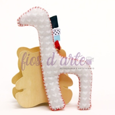 Peluche girafa branco com corações cinzentos e detalhes coloridos sobre suporte de madeira
