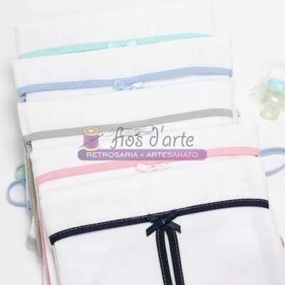 Conjunto de fraldas brancas com bordas coloridas e laços, e chupeta ao lado