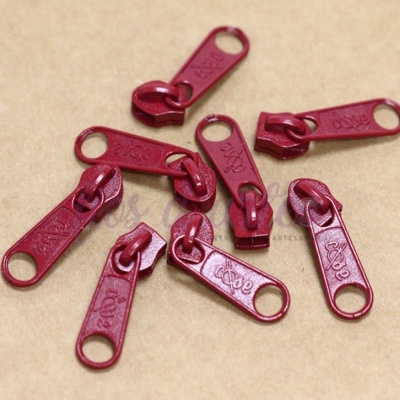 Puxadores de zíper vermelhos com texto YKK sobre superfície bege