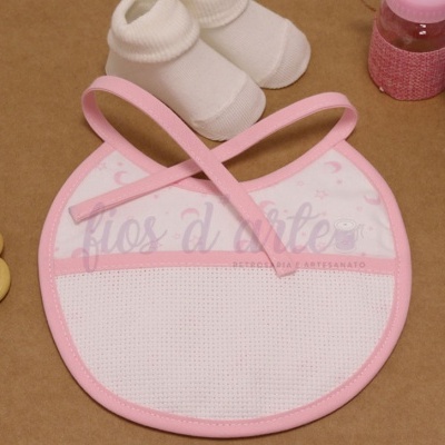 Babete de bebé redondo branco e rosa com meias brancas e brinquedos em fundo castanho