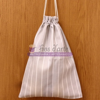 Saco de tecido com fecho de cordão pendurado em madeira com texto 'Fios d'arte RETROSARIA . ARTESANATO'