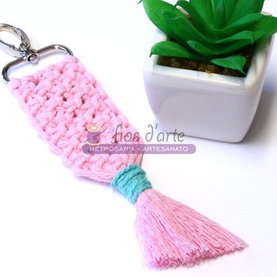 Chaveiro de crochê rosa com tassel, mosquetão metálico junto a vaso branco com planta verde
