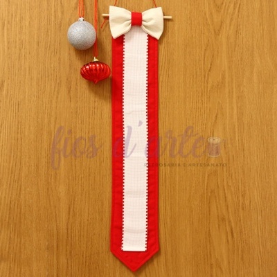 Gravata decorativa de feltro com laço pendurada numa parede de madeira com bolas de Natal