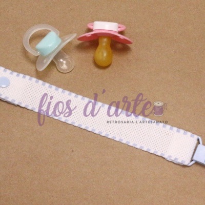 Dois chupetas e presa-chupetas branca com botões sobre fundo castanho claro