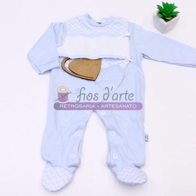 Macacão de bebé azul claro com padrão zig-zag e botões, ao lado de planta em vaso branco