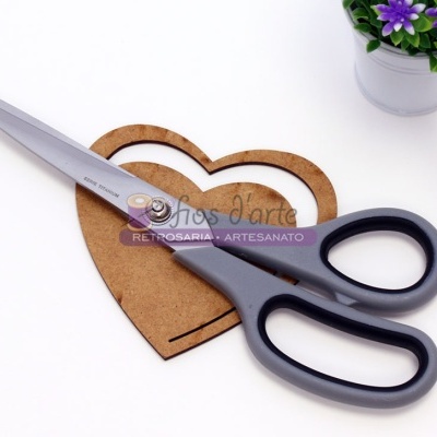 Tesoura preta e cinza sobre molde de coração em madeira com planta em vaso ao lado