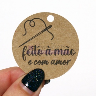Etiqueta redonda de papel com texto feito à mão e com amor, segurada por uma mão com unhas pintadas de preto com brilhos