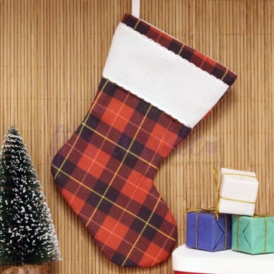 Meia de Natal xadrez vermelha com punho branco junto a árvore e caixas de presente pequenas