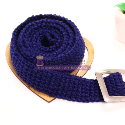 Cinto azul escuro trançado com fivela prateada sobre cartão castanho ao lado de planta em vaso branco